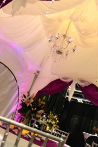 A WeatherPort Canopy at the 2015 Seattle Wedding Show is adorned with translucent fabric, hanging string lights and a chandelier.