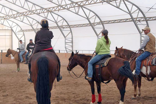 equestrians sitting atop horses in a weatherport sports facility